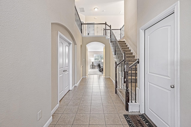 foyer featuring visible vents, baseboards, a high ceiling, light tile patterned flooring, and arched walkways