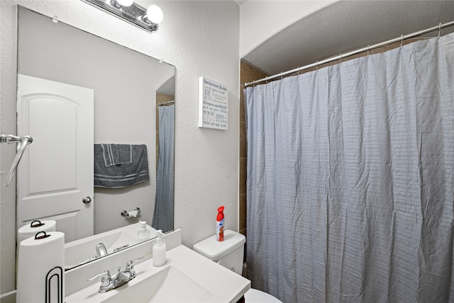 bathroom featuring curtained shower, toilet, vanity, and a textured wall