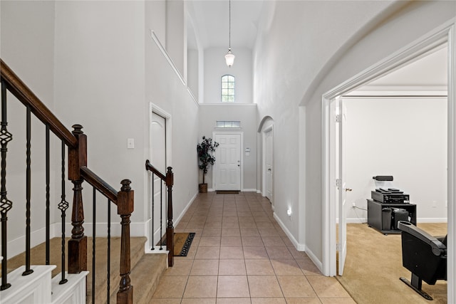 entrance foyer with light tile patterned floors, light colored carpet, baseboards, and a towering ceiling