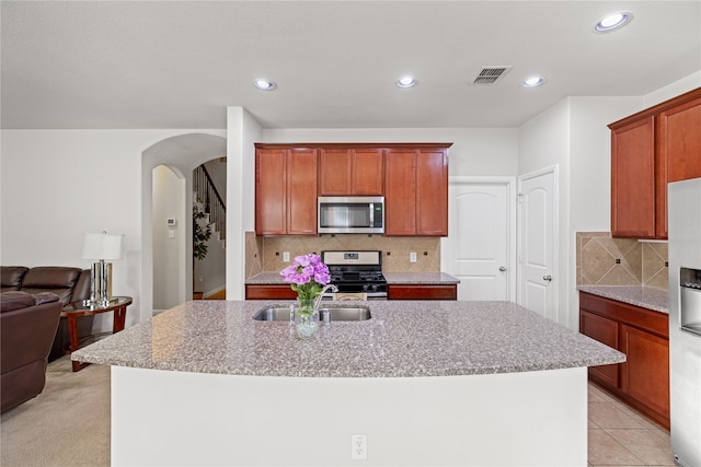 kitchen with visible vents, a center island with sink, a sink, stainless steel appliances, and arched walkways