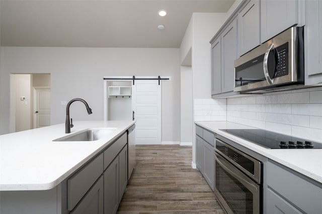 kitchen featuring dark hardwood / wood-style floors, sink, an island with sink, a barn door, and stainless steel appliances