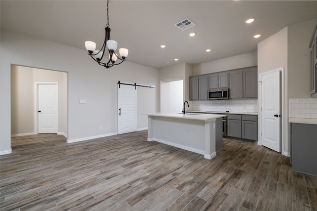 kitchen with gray cabinets, wood-type flooring, a kitchen island with sink, sink, and a barn door