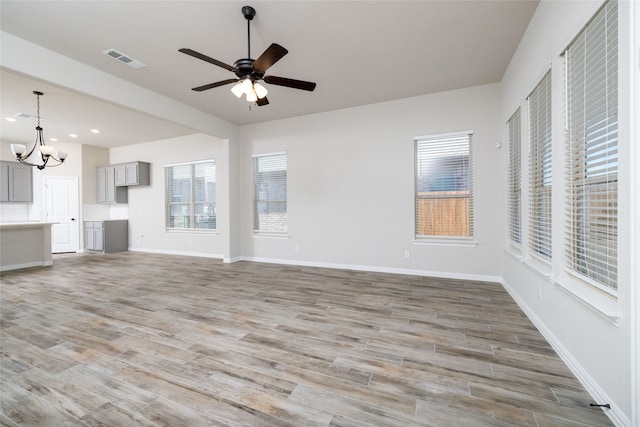 unfurnished living room with ceiling fan with notable chandelier and light wood-type flooring