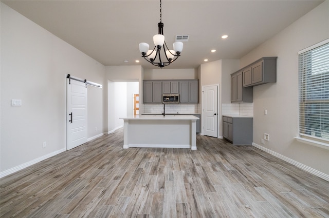 kitchen with an island with sink, light hardwood / wood-style floors, a barn door, and gray cabinetry