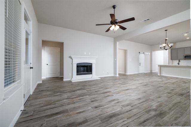 unfurnished living room with sink, ceiling fan with notable chandelier, hardwood / wood-style floors, and a barn door