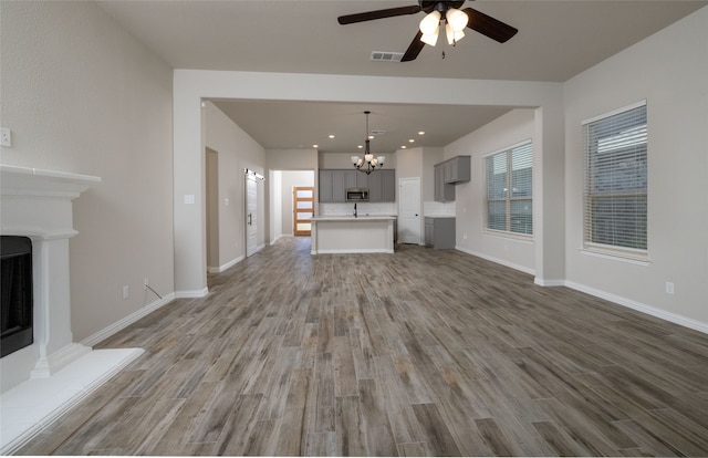 unfurnished living room featuring ceiling fan with notable chandelier and hardwood / wood-style floors