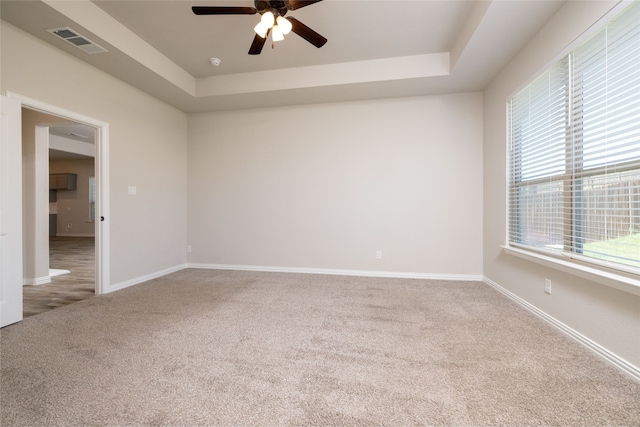 empty room with ceiling fan, a raised ceiling, and carpet