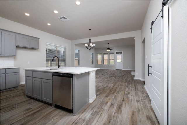 kitchen featuring sink, a kitchen island with sink, dishwasher, a barn door, and hardwood / wood-style floors