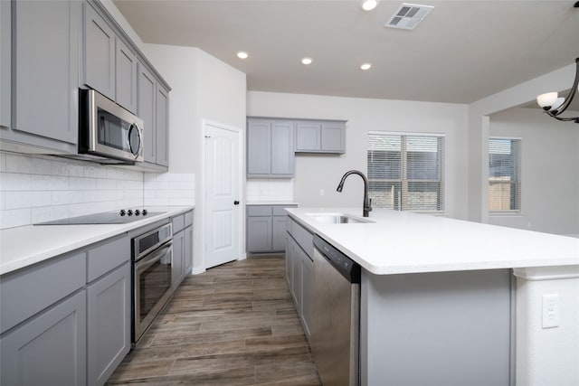 kitchen with sink, a kitchen island with sink, stainless steel appliances, dark hardwood / wood-style floors, and decorative backsplash