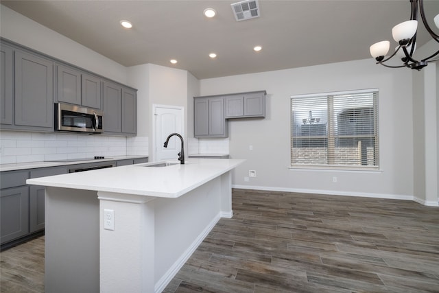 kitchen featuring an island with sink, tasteful backsplash, dark hardwood / wood-style flooring, gray cabinets, and sink