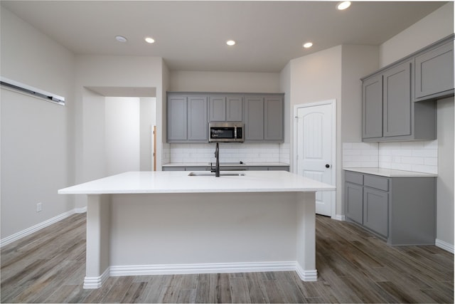 kitchen with gray cabinets, wood-type flooring, and a kitchen island with sink