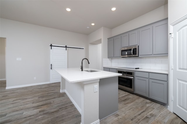 kitchen with sink, a barn door, light hardwood / wood-style flooring, stainless steel appliances, and a center island with sink