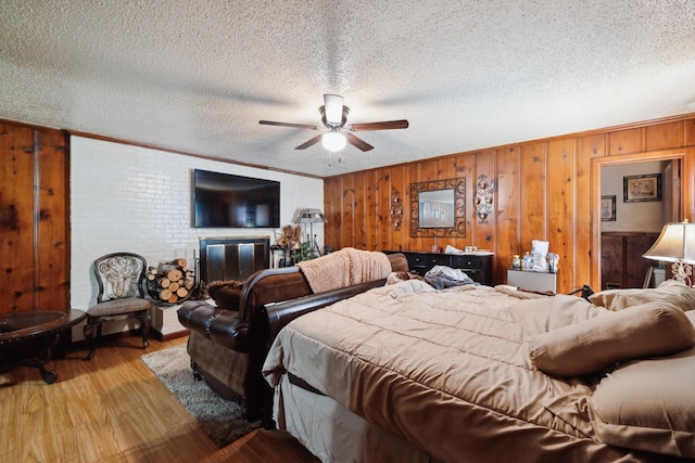 bedroom with a textured ceiling, wood walls, wood finished floors, crown molding, and a brick fireplace
