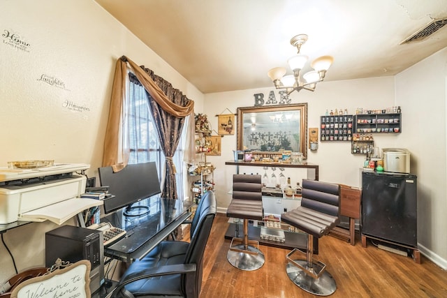 office space featuring baseboards, wood finished floors, visible vents, and an inviting chandelier