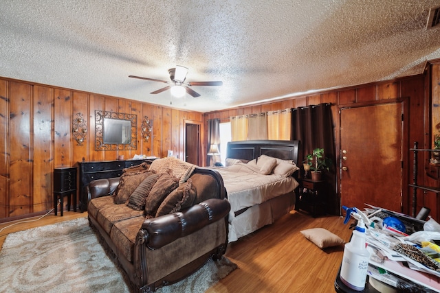 bedroom with wood-type flooring, a textured ceiling, ceiling fan, and wooden walls