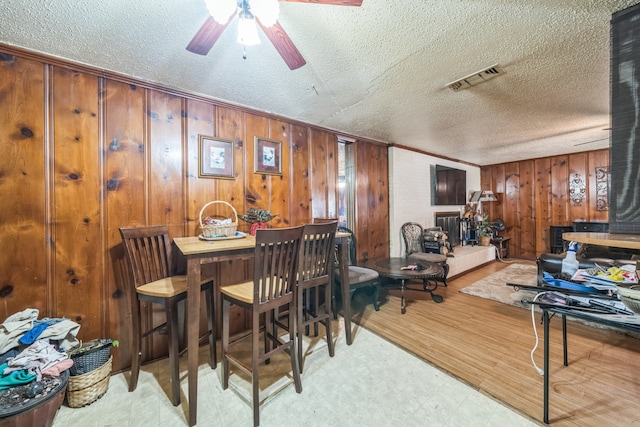 dining area with a textured ceiling, wooden walls, and ceiling fan