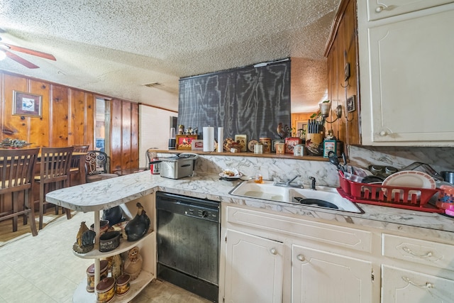 kitchen with ceiling fan, sink, a textured ceiling, wooden walls, and black dishwasher