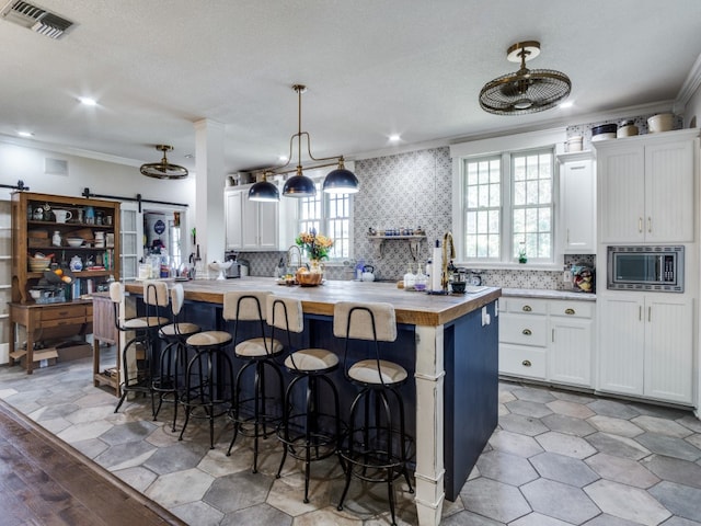 kitchen featuring hanging light fixtures, white cabinetry, a barn door, a kitchen island, and crown molding