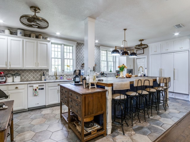 kitchen featuring hanging light fixtures, white cabinets, white dishwasher, crown molding, and a kitchen island with sink