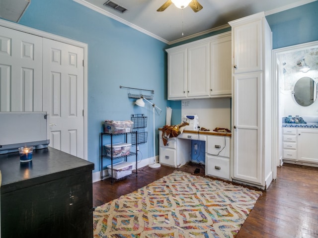 office space with ceiling fan, built in desk, crown molding, and dark wood-type flooring