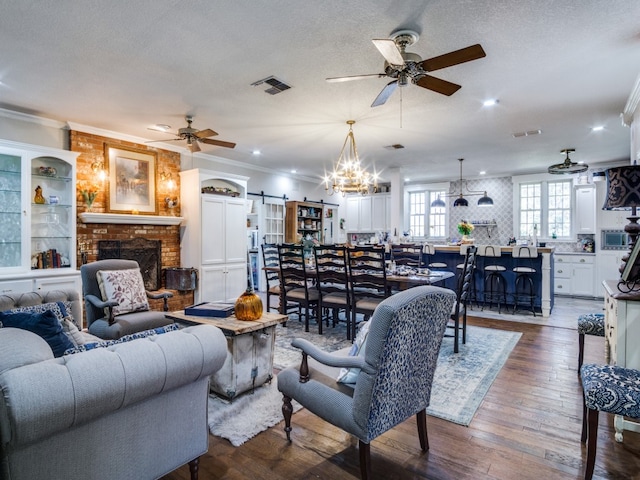 living room featuring a textured ceiling, dark wood-type flooring, a fireplace, a barn door, and ornamental molding