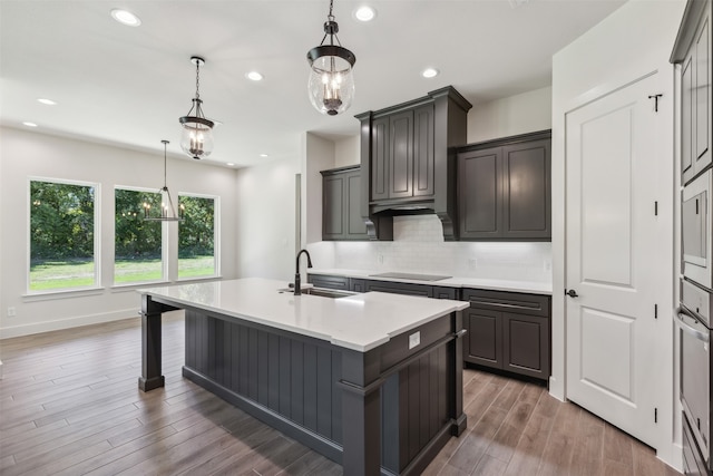 kitchen featuring an island with sink, hanging light fixtures, sink, dark hardwood / wood-style flooring, and decorative backsplash