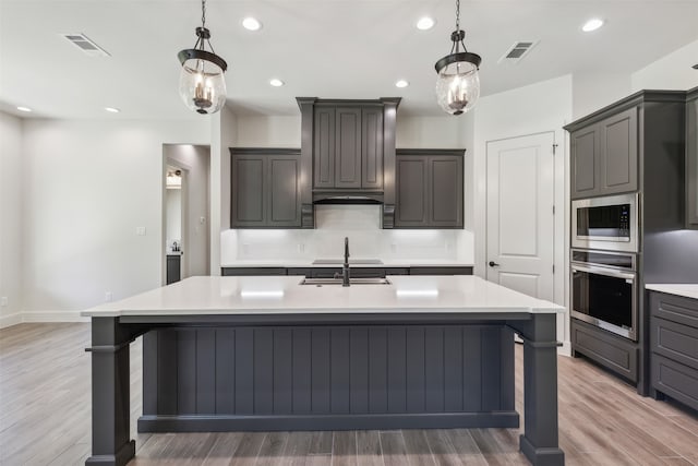 kitchen featuring a large island with sink, light hardwood / wood-style flooring, stainless steel appliances, and decorative light fixtures