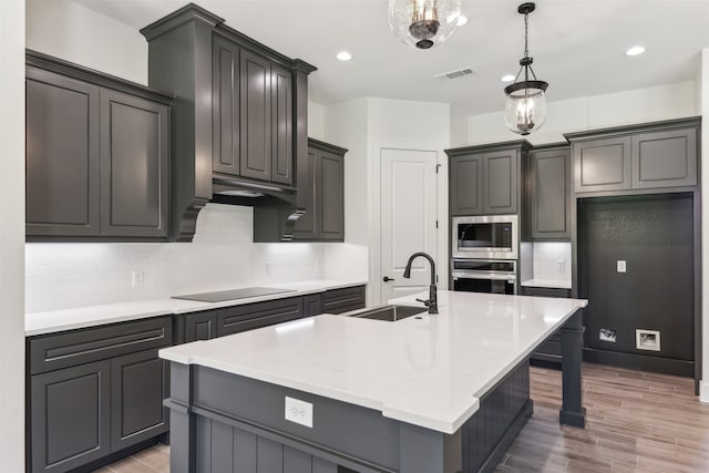 kitchen featuring light wood-type flooring, sink, an island with sink, appliances with stainless steel finishes, and decorative light fixtures