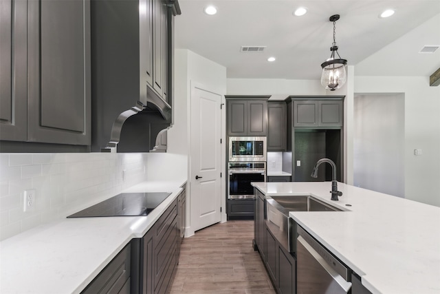 kitchen with tasteful backsplash, sink, stainless steel appliances, decorative light fixtures, and hardwood / wood-style floors