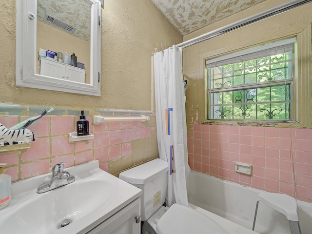 full bathroom with vanity, tile walls, shower / bath combo with shower curtain, and toilet