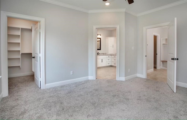 unfurnished bedroom with ceiling fan, a spacious closet, light colored carpet, crown molding, and ensuite bathroom