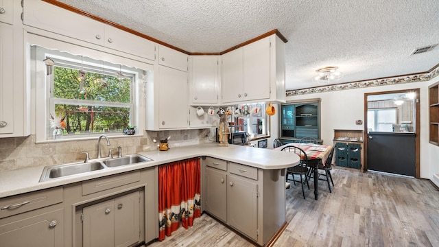 kitchen featuring light wood finished floors, visible vents, light countertops, a peninsula, and a sink