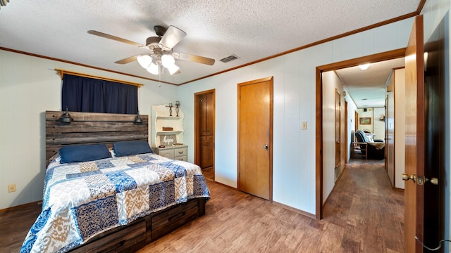 bedroom featuring visible vents, ornamental molding, a textured ceiling, wood finished floors, and ceiling fan