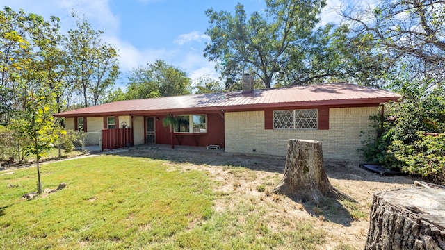 view of front facade featuring brick siding, a chimney, a front lawn, and metal roof