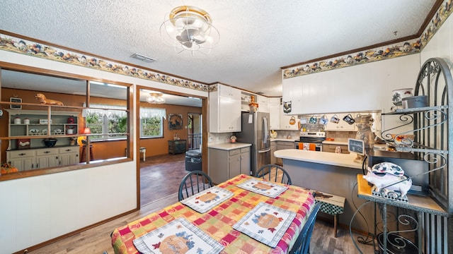 dining space featuring visible vents, a textured ceiling, wood finished floors, and ornamental molding