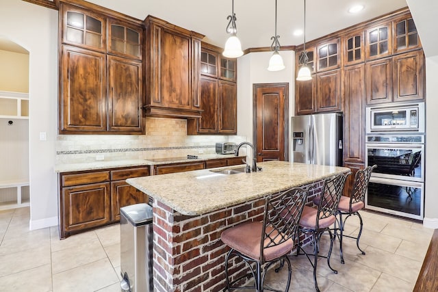 kitchen with sink, a kitchen island with sink, decorative light fixtures, appliances with stainless steel finishes, and light stone countertops