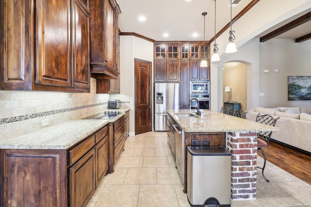 kitchen featuring pendant lighting, a kitchen breakfast bar, a center island with sink, appliances with stainless steel finishes, and light stone countertops