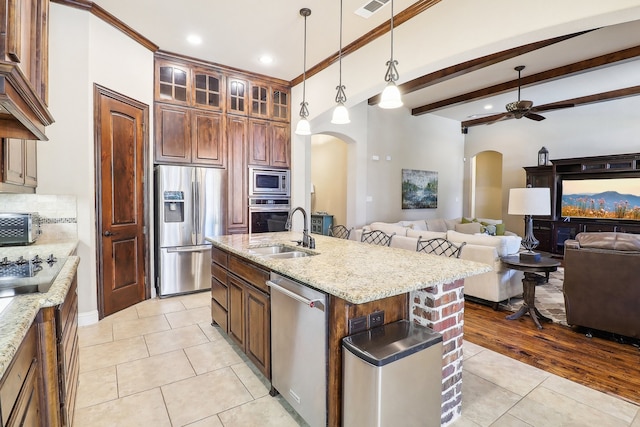 kitchen with an island with sink, sink, decorative light fixtures, appliances with stainless steel finishes, and light wood-type flooring