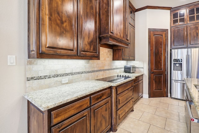 kitchen featuring stainless steel fridge, light stone counters, backsplash, light tile patterned floors, and black electric stovetop