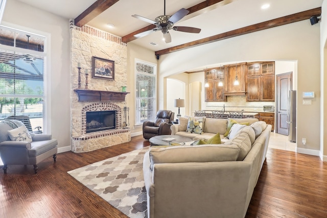 living room featuring ceiling fan, dark wood-type flooring, a fireplace, and beam ceiling