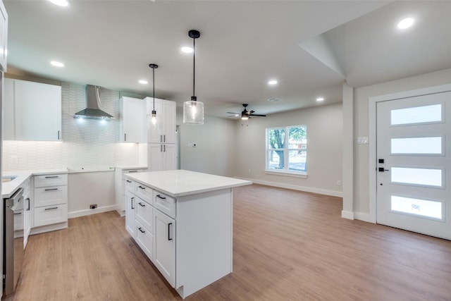 kitchen featuring decorative backsplash, light wood-type flooring, wall chimney range hood, white cabinetry, and hanging light fixtures