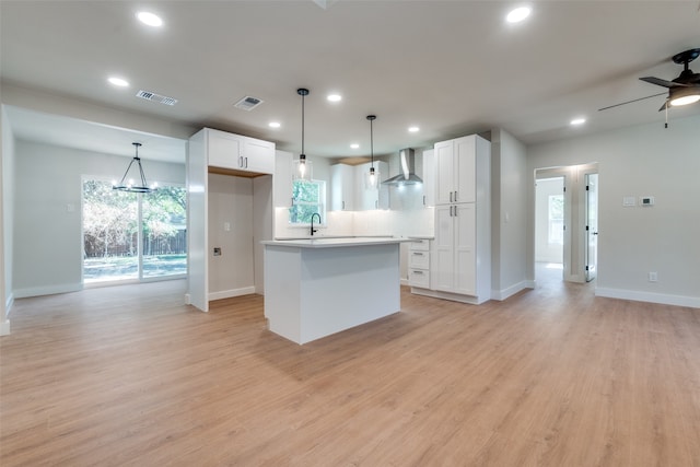 kitchen with white cabinets, a center island, wall chimney range hood, and light hardwood / wood-style floors