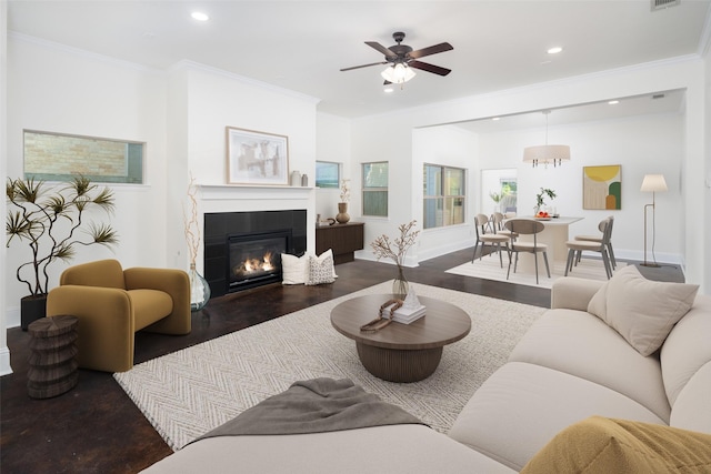 living room with ceiling fan, a tiled fireplace, crown molding, and dark wood-type flooring