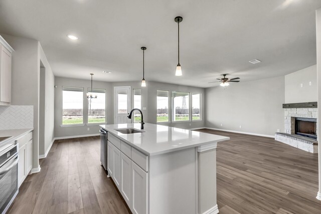 kitchen featuring ceiling fan with notable chandelier, sink, white cabinetry, a stone fireplace, and an island with sink