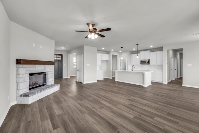 unfurnished living room with ceiling fan, a fireplace, dark hardwood / wood-style floors, and sink