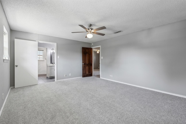 unfurnished bedroom with light carpet, ensuite bath, ceiling fan, and a textured ceiling