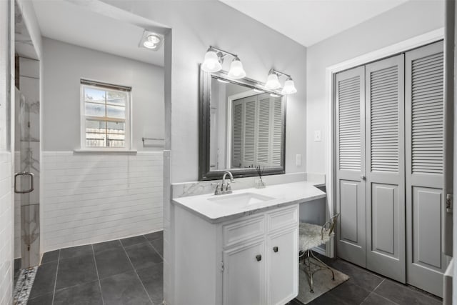 bathroom with tile patterned floors, a shower with door, vanity, and tile walls