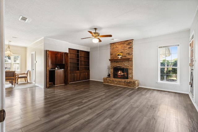 unfurnished living room with dark wood-type flooring, visible vents, ceiling fan, and a brick fireplace