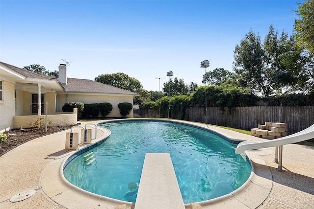 view of swimming pool featuring a patio, a water slide, and a diving board