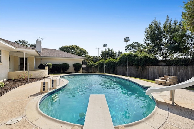 view of swimming pool with a water slide, a fenced in pool, a fenced backyard, and a diving board